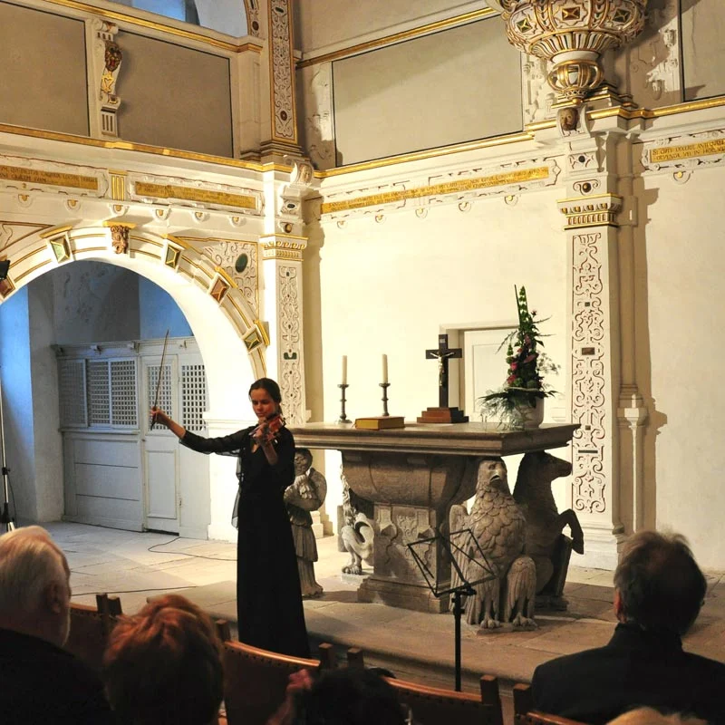 Eine Musikerin vor Publikum in einem Saal von Schloss Wilhelmsburg.