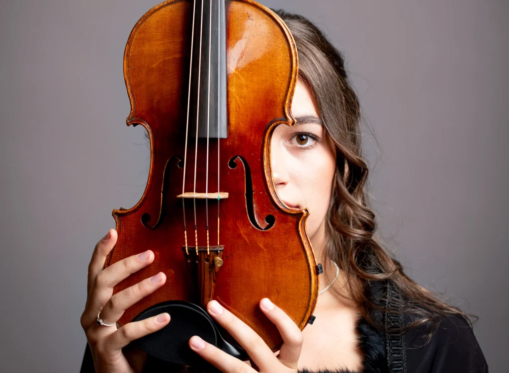 Eine Geigerin hält ihre Violine vor das Gesicht, ein Auge schaut hervor.